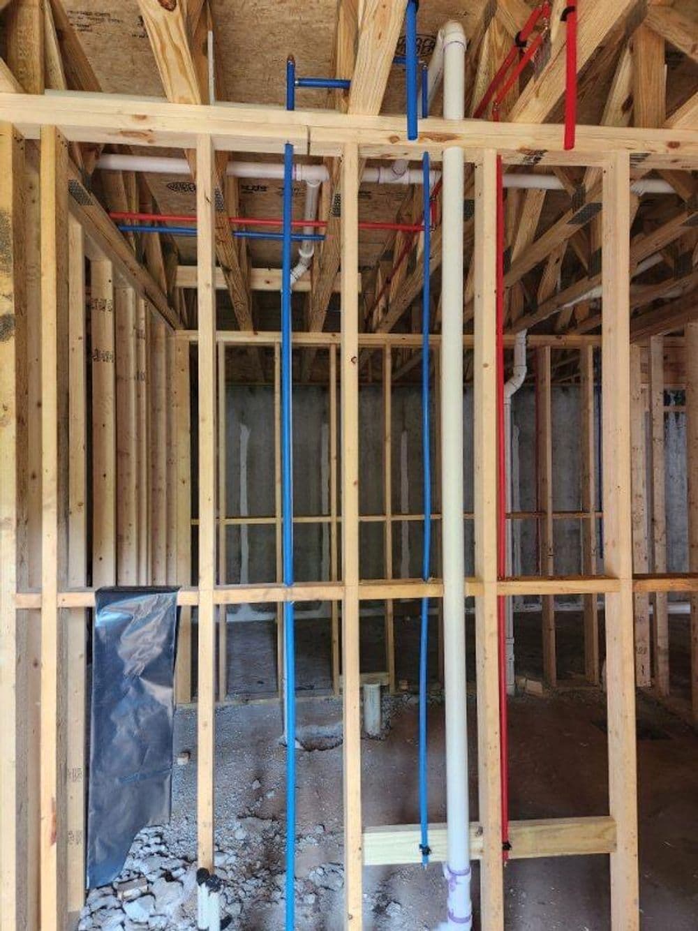 Water and drainage pipes installed in wooden framing of a construction site interior.