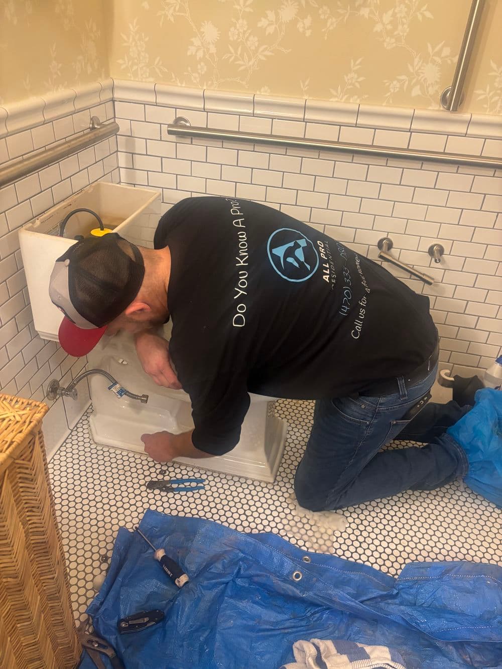 Plumber repairing a bathtub in a vintage bathroom with white tile and black accents.