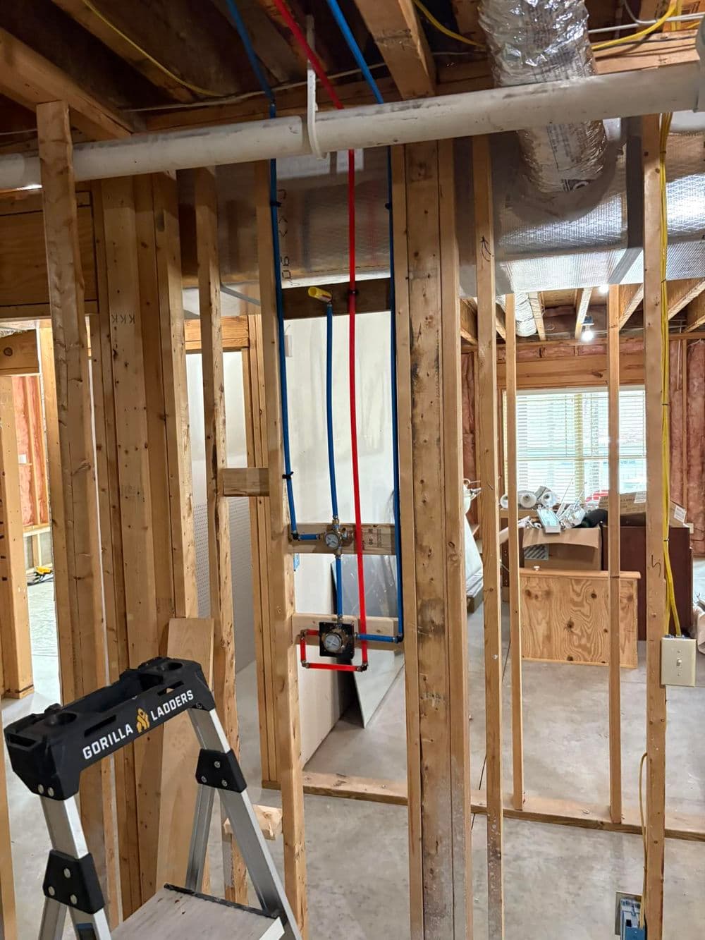 Construction site showing exposed framing, plumbing, and a ladder in a partially finished room.